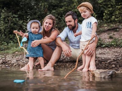 A young family with two toddler children outdoors by the river in summer.