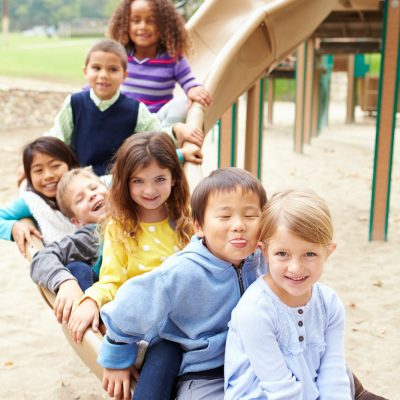 Group Of Young Children Sitting On Slide In Playground
