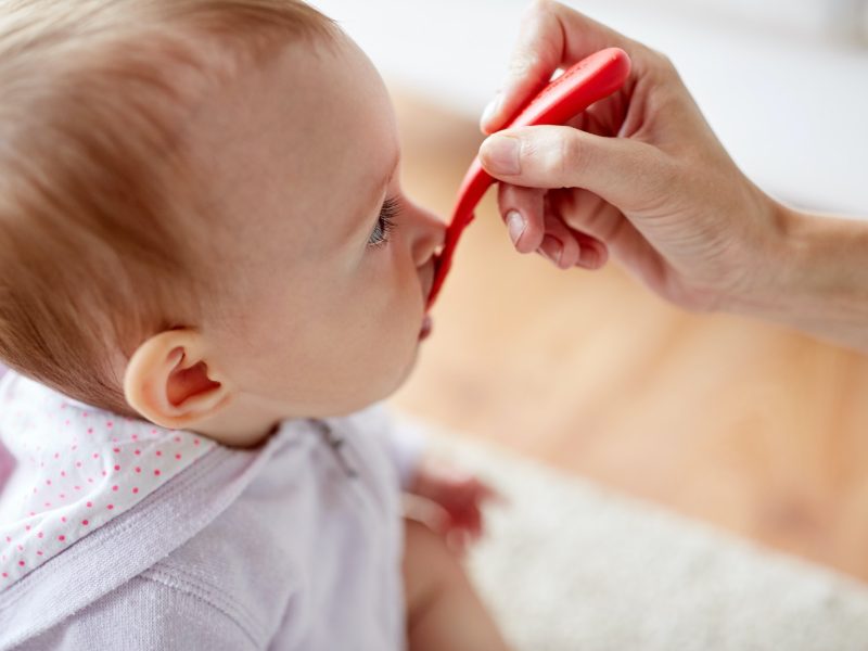 hand with spoon feeding little baby at home