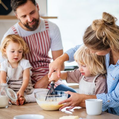 Young family with two small children indoors in kitchen, cooking.